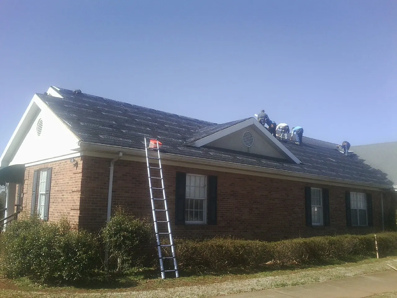 Crew tearing shingles off a brick ranch roof with a ladder set — Metal Roof Repair work by our crew in Aberdeen