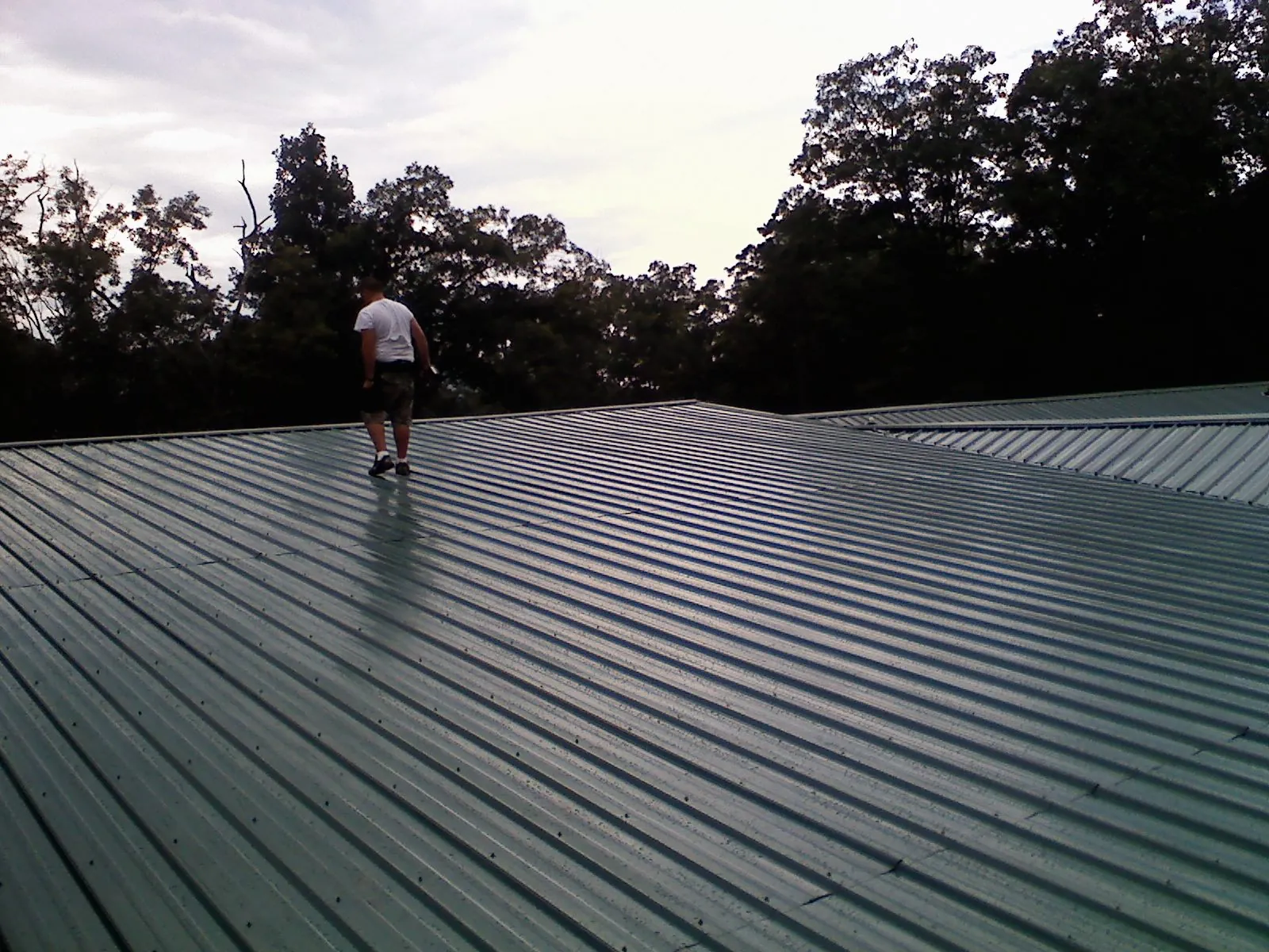 Roofer walking a wide expanse of new green metal roofing in Aberdeen
